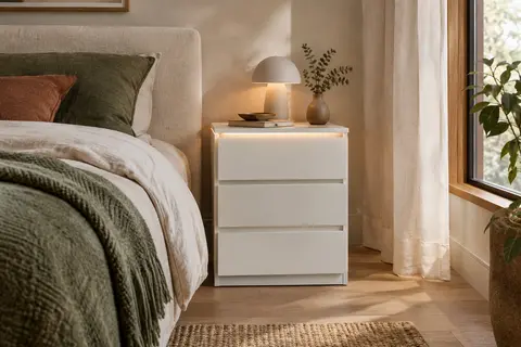 Table de chevet blanche à trois tiroirs avec éclairage LED, installée dans une chambre aux matières naturelles.